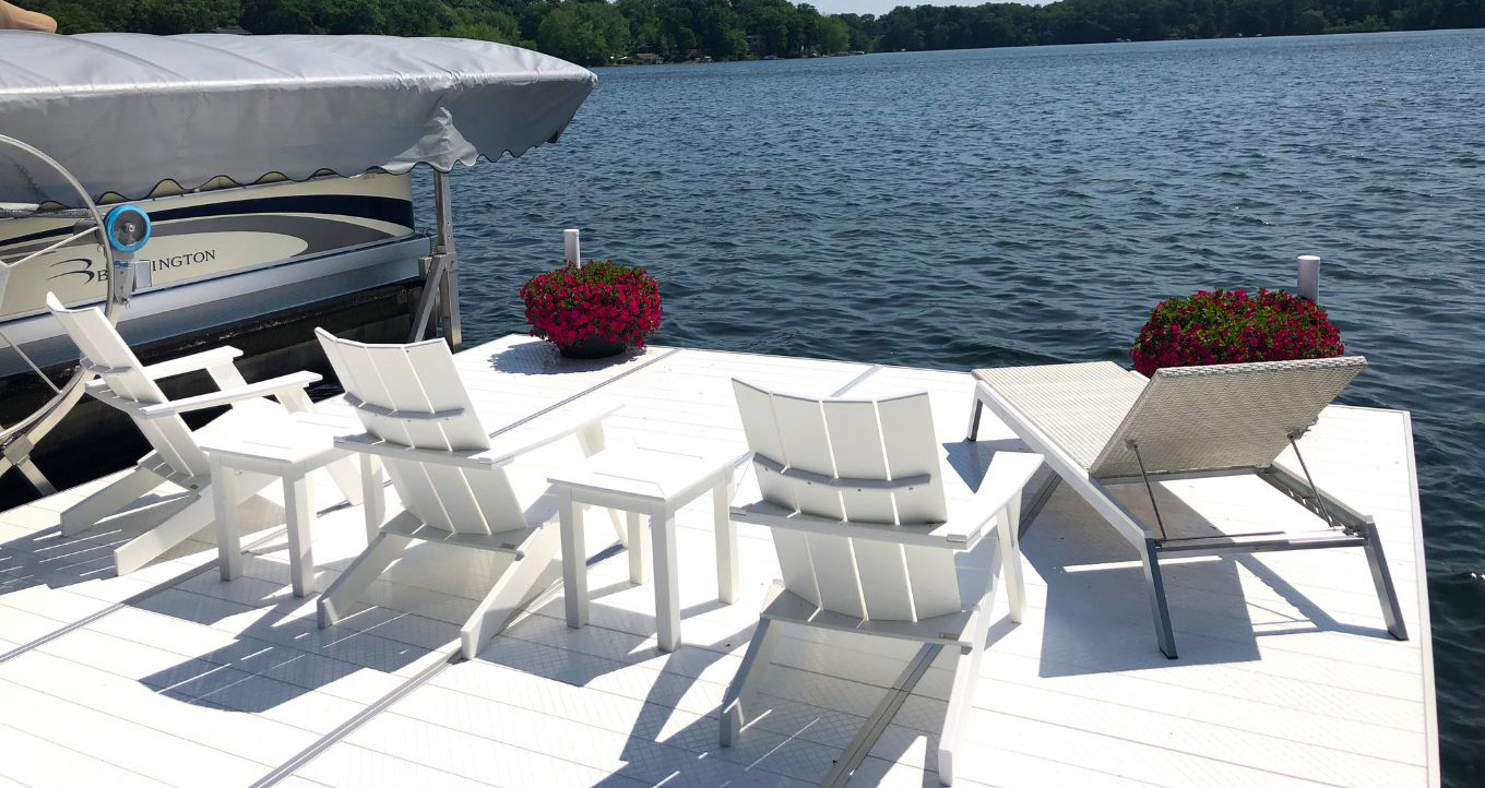 White Adirondack chair on a white deck on a blue lake.